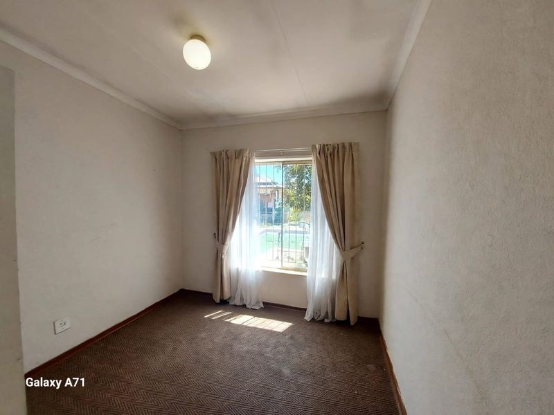 An empty bedroom featuring carpeted flooring, a window with security bars, and neutral wall finishes, offering a blank canvas for potential updates.