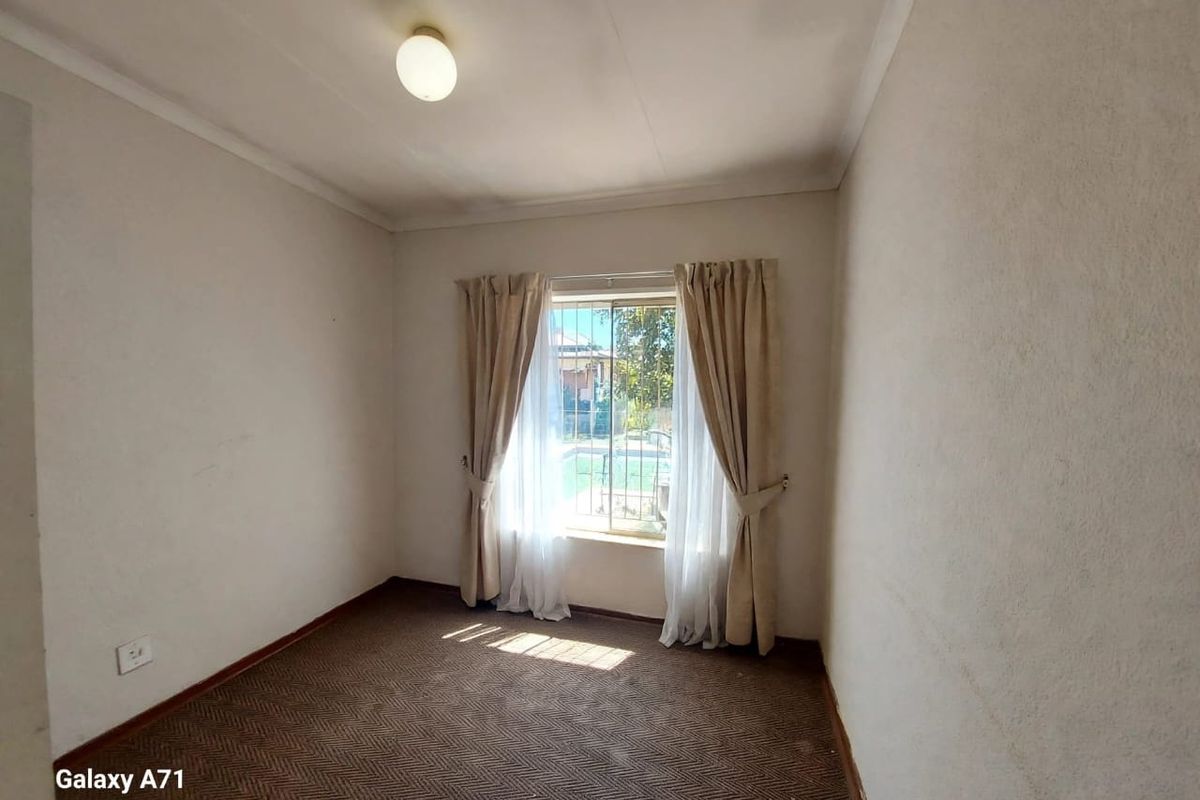 An empty bedroom featuring carpeted flooring, a window with security bars, and neutral wall finishes, offering a blank canvas for potential updates.