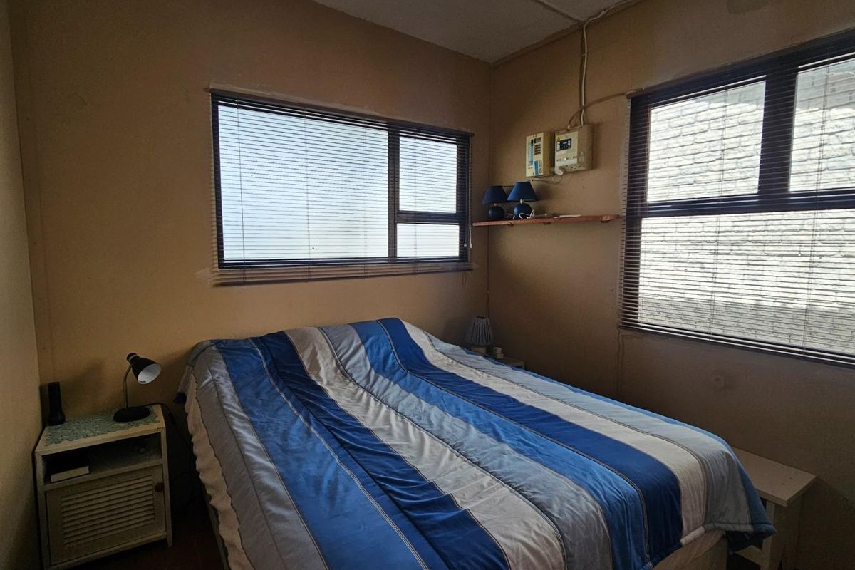 A bedroom featuring dual windows with fitted blinds and exposed electrical infrastructure on the wall.