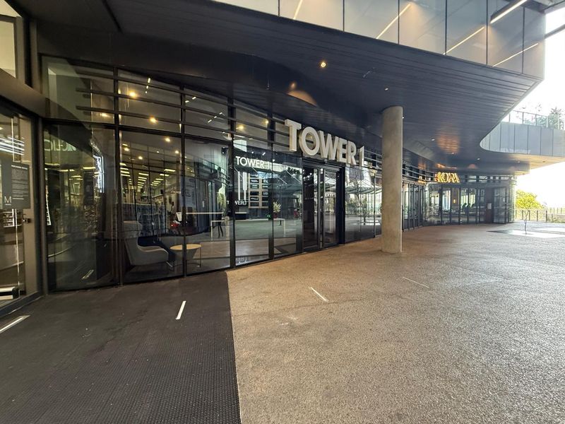 Modern commercial office building entrance featuring a glass facade, covered walkway, and prominent Tower 1 signage.