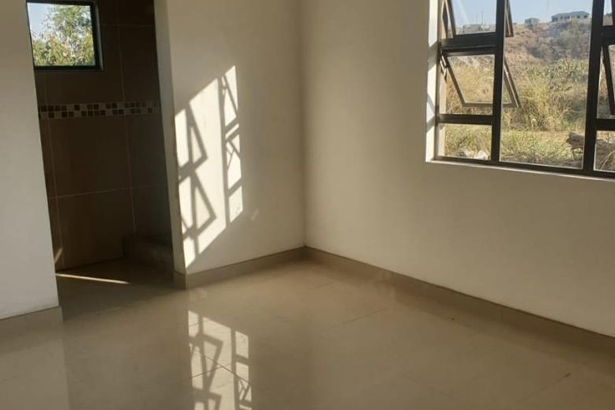 A bright, empty bedroom featuring neutral tiled flooring, clean white walls, and aluminium-framed windows with natural light.