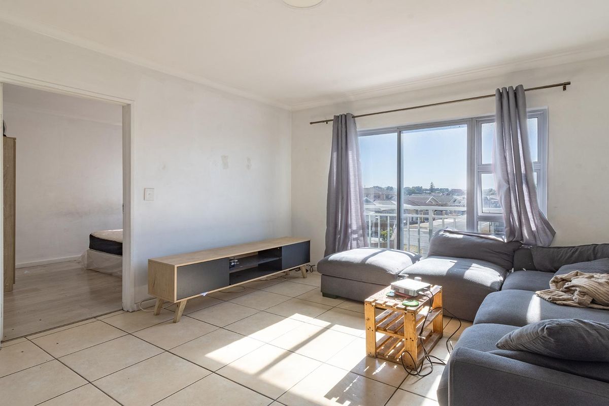 A bright living room featuring tiled flooring and a large sliding glass door providing access to a balcony with neighborhood views.