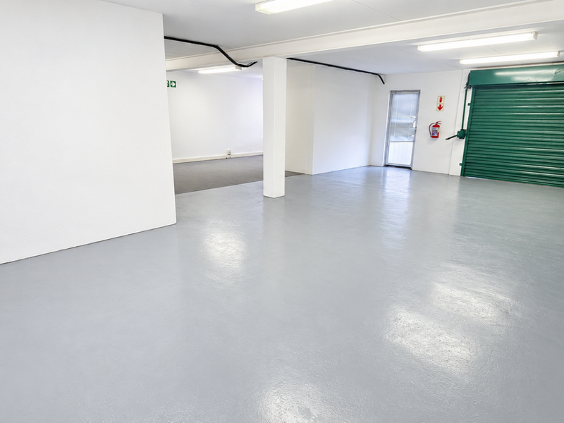 Spacious industrial garage featuring a durable epoxy-coated floor, secure green roller shutter door, and bright overhead fluorescent lighting.