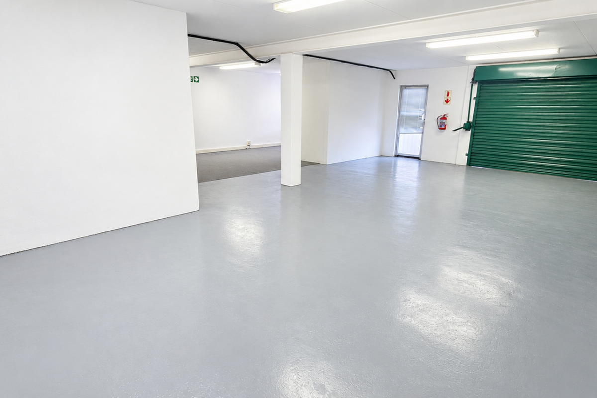 Spacious industrial garage featuring a durable epoxy-coated floor, secure green roller shutter door, and bright overhead fluorescent lighting.