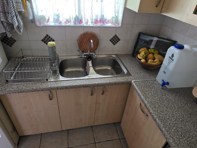 A functional kitchen area featuring a double bowl stainless steel sink, laminate countertops, and tiled backsplash with built-in cabinetry.