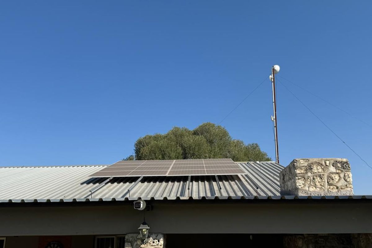 Rear view of the farm property featuring a corrugated metal roof with installed solar panels, a stone chimney, and a communication mast.
