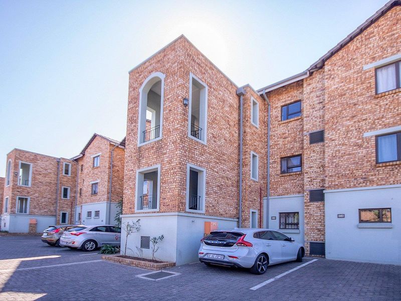 Exterior view of a multi-story townhouse complex featuring face brick construction, paved parking areas, and integrated balconies.