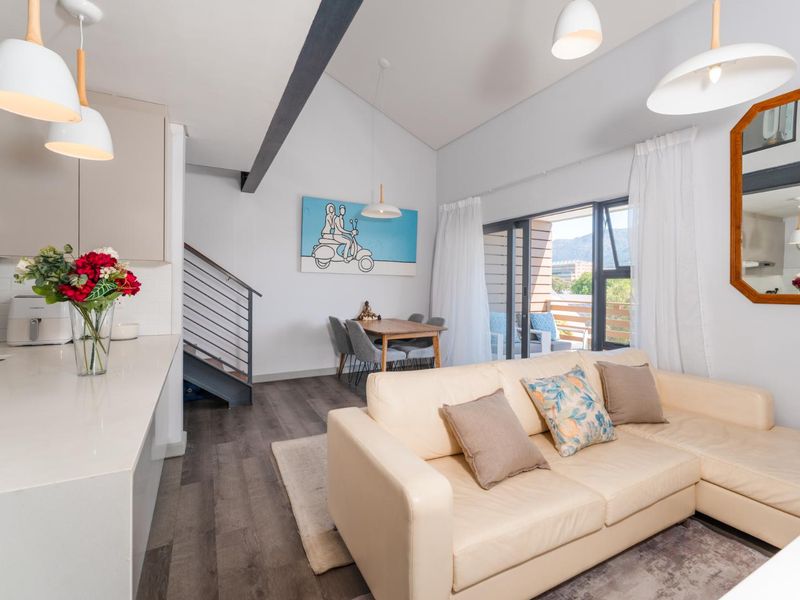 Bright open-plan living area featuring a modern kitchen with stone countertops, vaulted ceilings with exposed beams, and direct access to a private balcony.