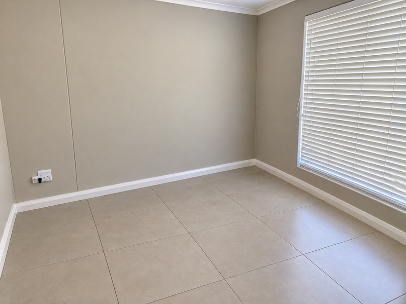 A clean, empty bedroom featuring neutral-toned tiled flooring, crisp white skirting boards, and fitted venetian blinds.