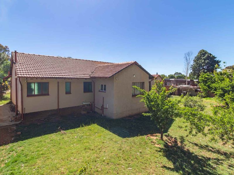 Rear view of the house featuring a tiled roof, plastered exterior walls, and a spacious garden area.
