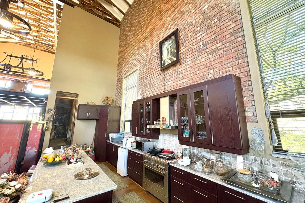 Spacious kitchen featuring high vaulted ceilings with exposed timber trusses, dark wood cabinetry, granite countertops, and a striking exposed brick feature wall.
