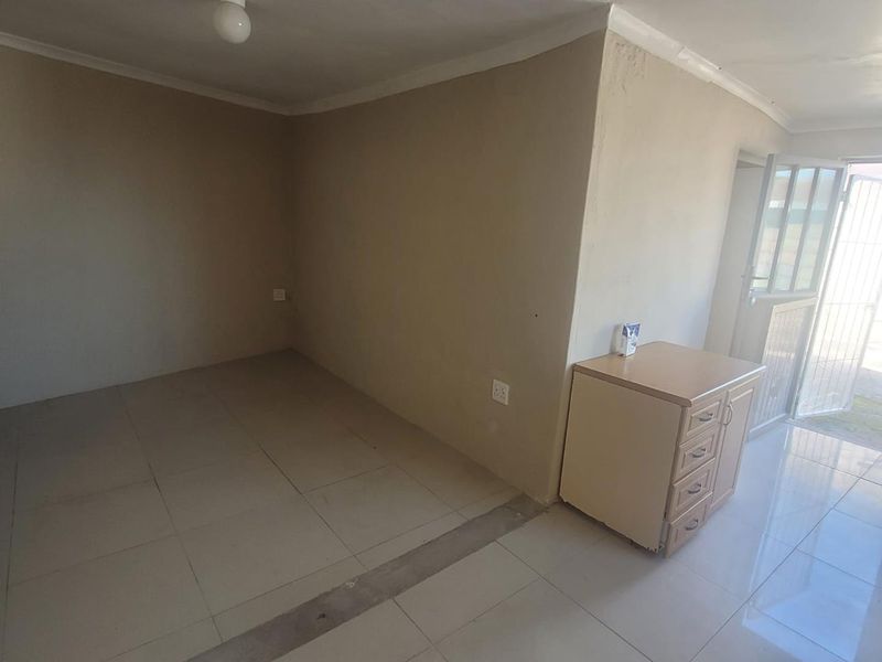 An empty living area featuring tiled flooring, neutral walls, and direct access to the exterior through a security gate.