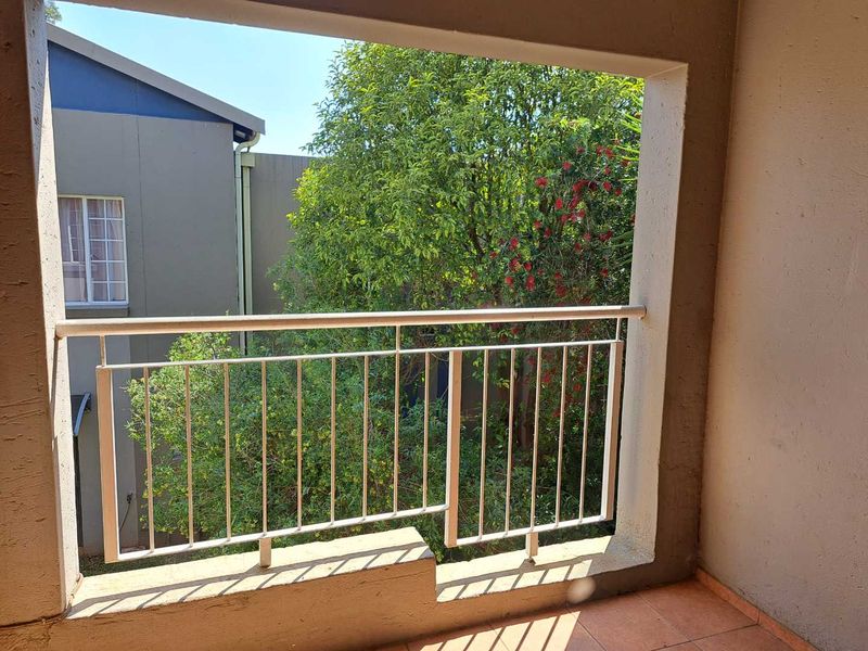 A covered balcony featuring a metal balustrade and tiled flooring, overlooking a garden area.