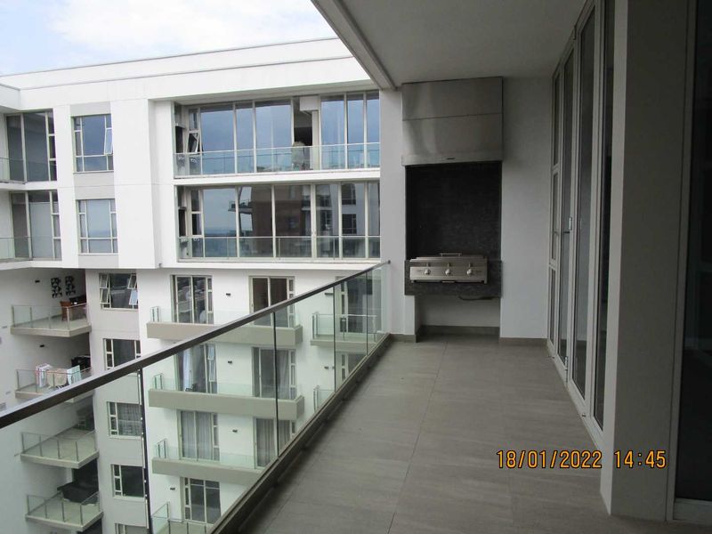 Spacious penthouse balcony featuring a built-in gas braai with stainless steel extractor, glass balustrade, and large sliding doors providing seamless indoor-outdoor flow.
