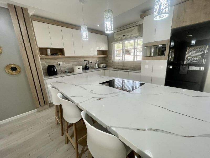 Modern kitchen featuring a large stone-topped island, high-gloss cabinetry, integrated appliances, and contemporary lighting, offering a sleek and functional culinary space.