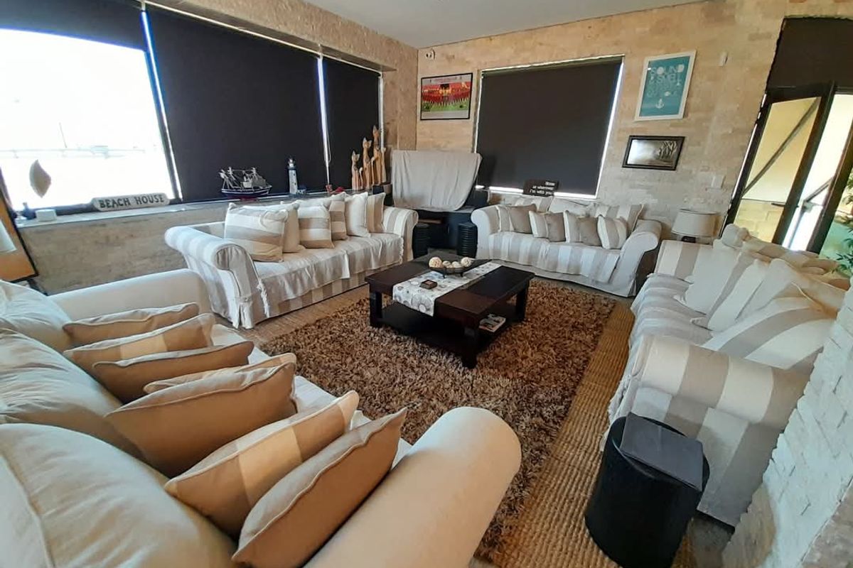 Spacious living room featuring natural stone wall cladding, large windows with roller blinds, and tiled flooring.