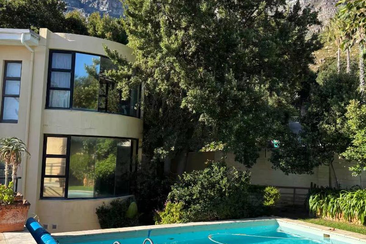 A private swimming pool set in a landscaped garden with a view of the mountain, featuring a curved building facade with large windows.