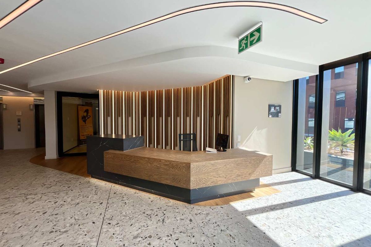 Modern office reception area featuring a custom built-in desk, elegant terrazzo flooring, and decorative slatted timber wall paneling with integrated lighting.