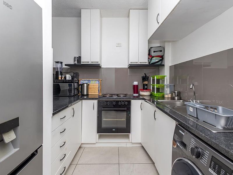 A compact, functional kitchen featuring white cabinetry, dark granite countertops, a built-in oven, electric hob, and tiled flooring.