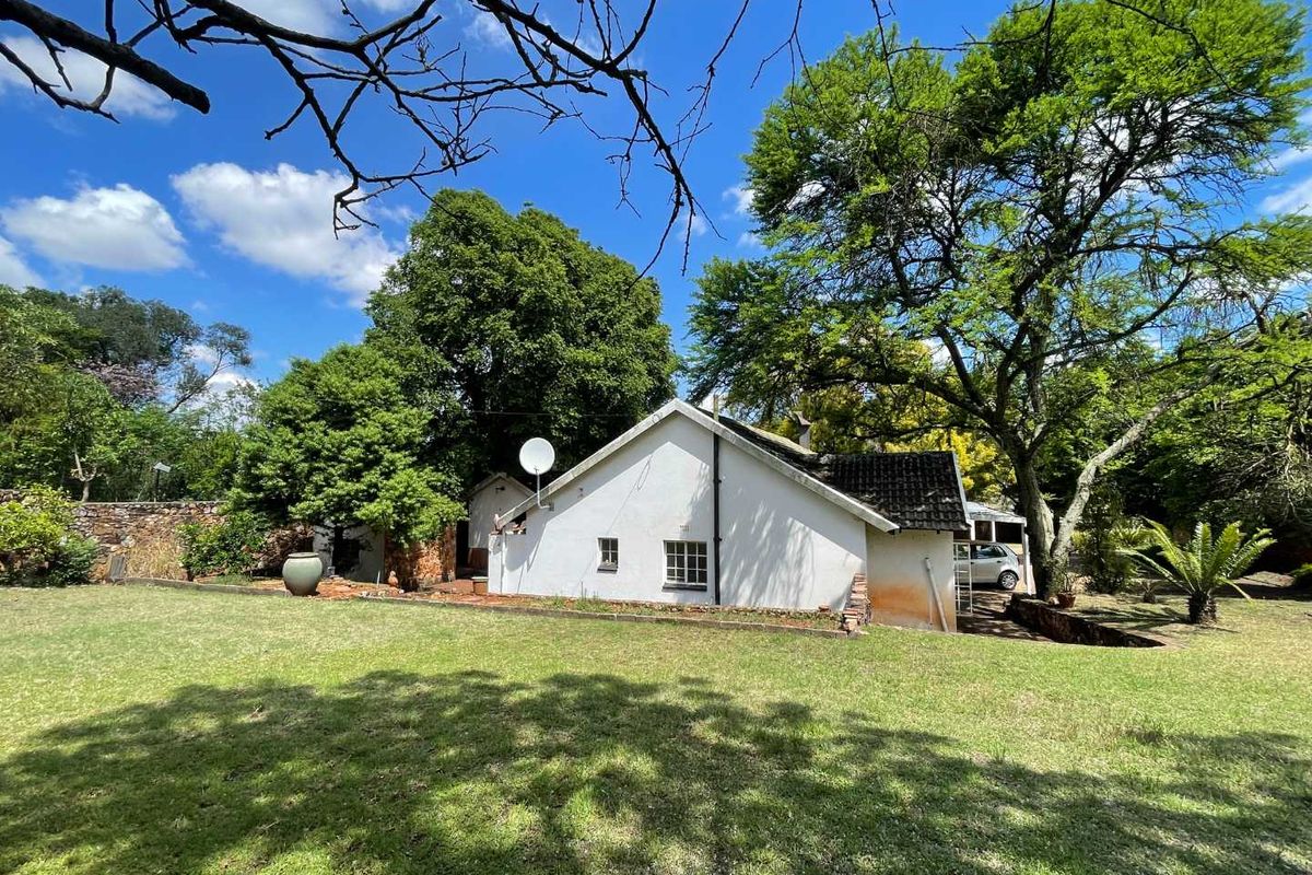 Rear view of the property featuring a white exterior, tiled roof, and a spacious, well-established garden with mature trees and stone boundary walls.