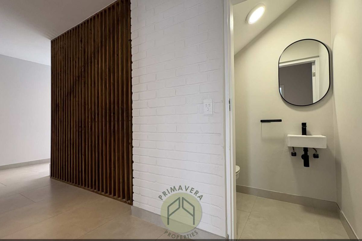 A modern guest bathroom featuring a wall-mounted basin, black fixtures, and a decorative timber slat feature wall in the adjacent hallway.