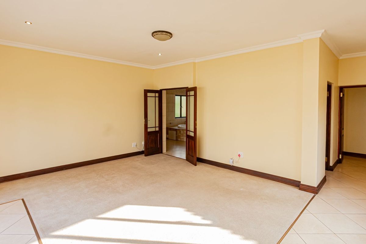 Spacious bedroom featuring neutral carpeting, recessed lighting, and double doors leading to an en-suite bathroom with tiled flooring.