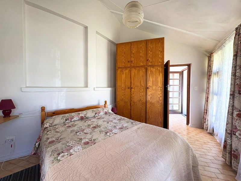 A bedroom featuring a vaulted ceiling, built-in wooden wardrobe, tiled flooring, and recessed wall niches, offering a functional space with potential for modernization.