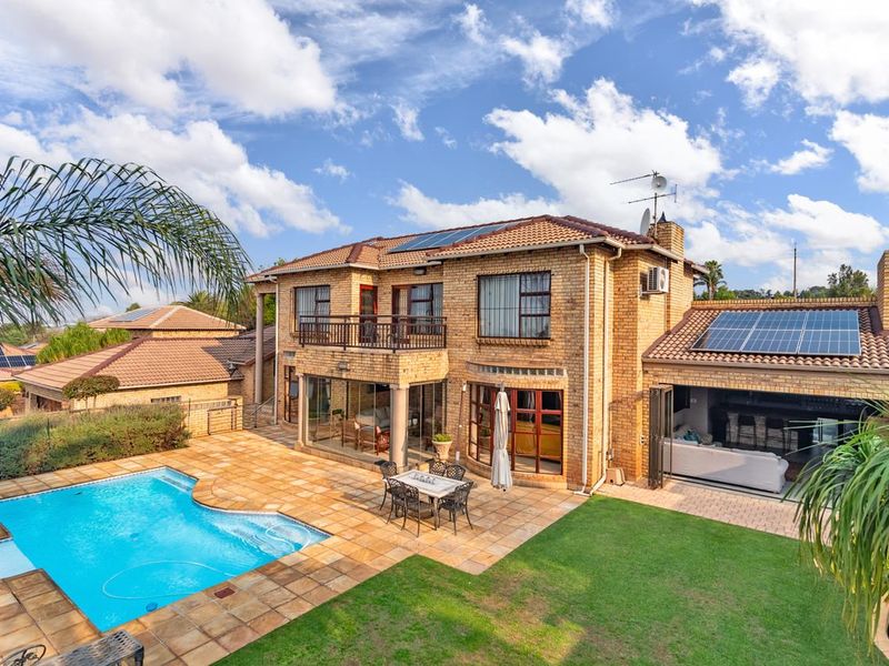 Rear view of a double-story brick house featuring a swimming pool, paved patio area, balcony, and roof-mounted solar panels.