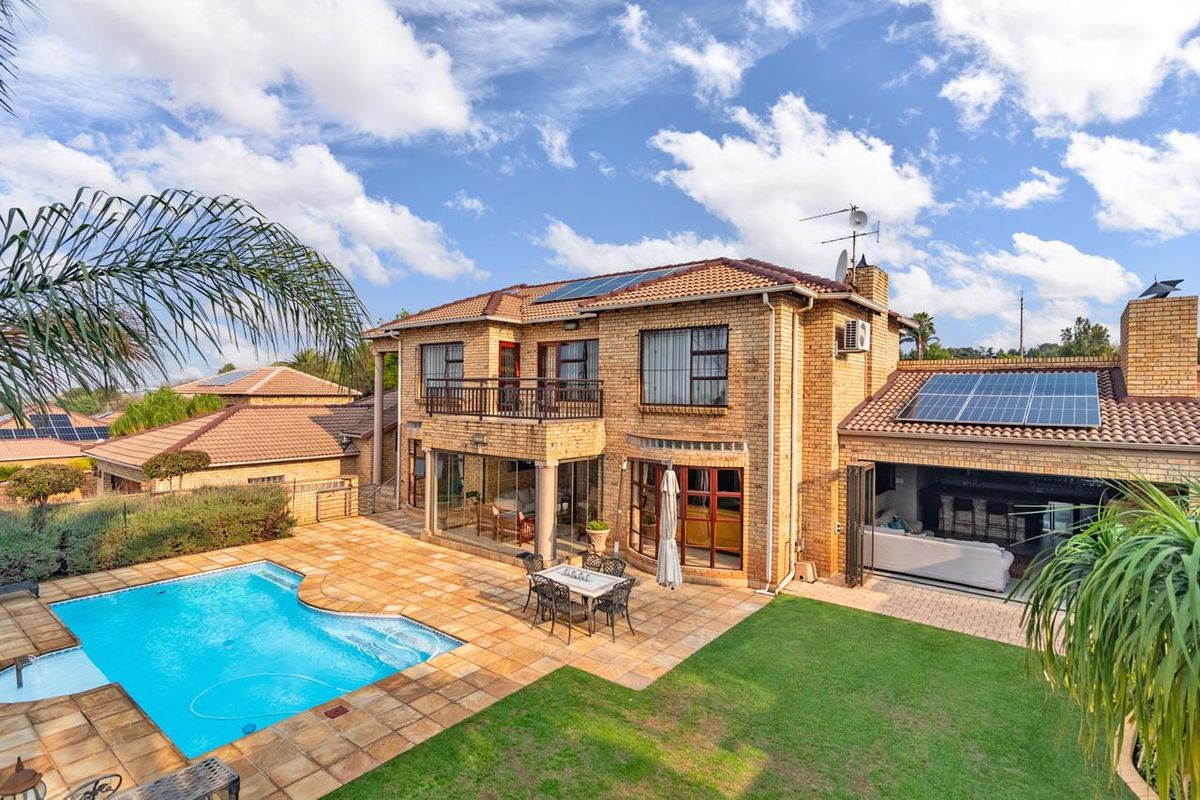 Rear view of a double-story brick house featuring a swimming pool, paved patio area, balcony, and roof-mounted solar panels.
