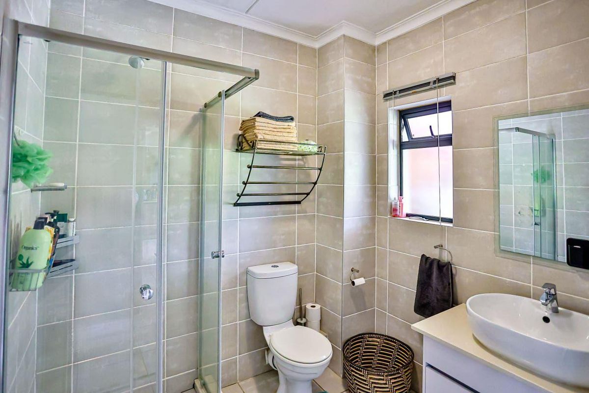 A well-maintained bathroom featuring a glass shower enclosure, neutral ceramic tiling, a modern vessel sink vanity, and a functional top-hung window.