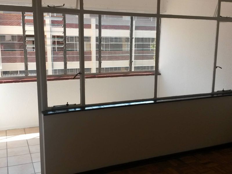 An enclosed balcony area featuring tiled flooring and large metal-framed windows, offering a bright and functional space for potential renovation.