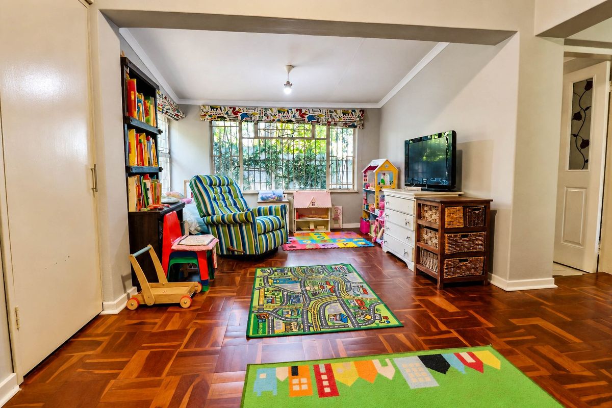 A versatile living area featuring classic parquet flooring, coved cornicing, and large windows fitted with security bars for added peace of mind.