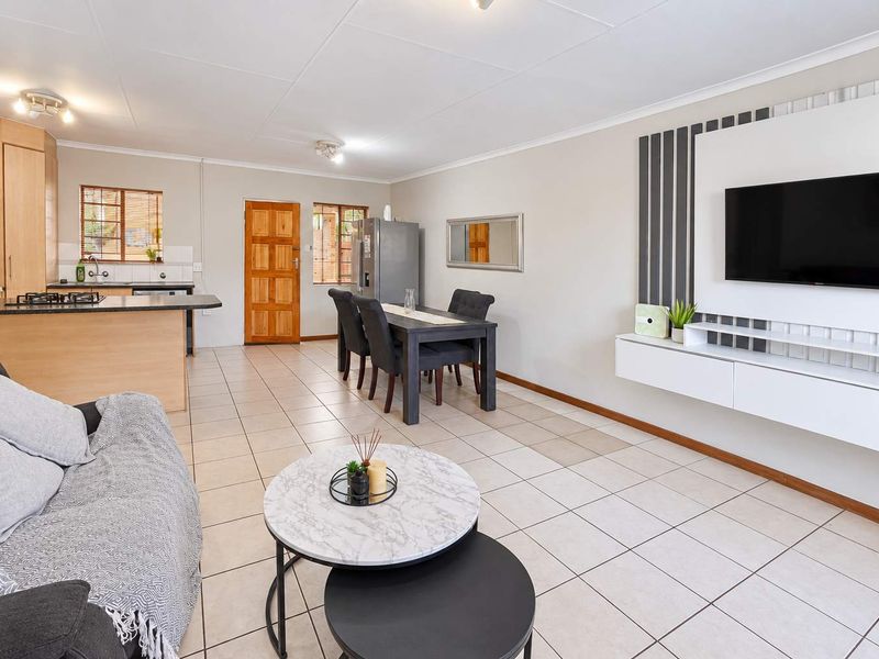 Open-plan living and dining area featuring tiled floors, a functional kitchen with island, and a modern built-in wall unit for entertainment.