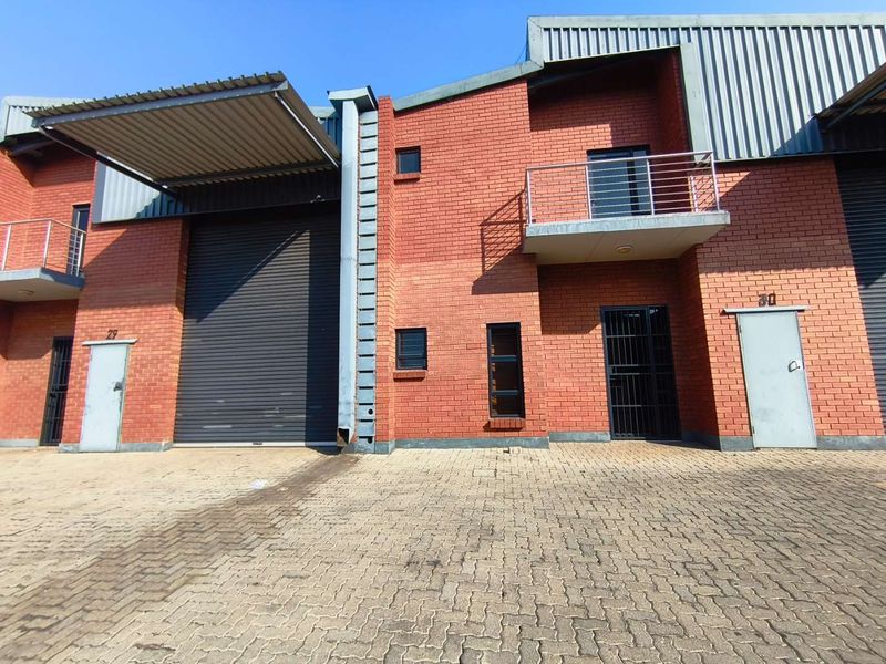 Front elevation of an industrial unit featuring a roller shutter door, brick facade, and a small balcony with steel railings.