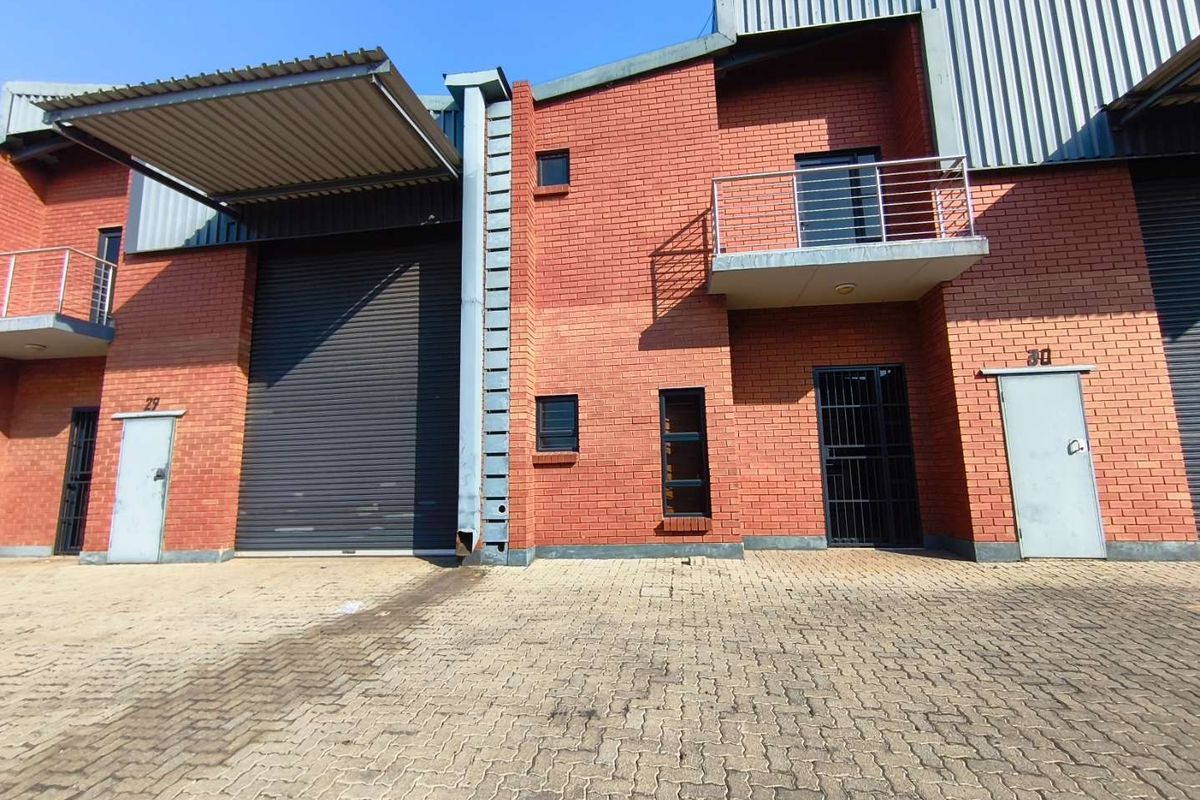 Front elevation of an industrial unit featuring a roller shutter door, brick facade, and a small balcony with steel railings.