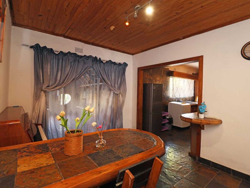 Open plan living and dining area featuring rustic slate tile flooring and a warm timber-clad ceiling, with an adjacent kitchen visible through the archway.