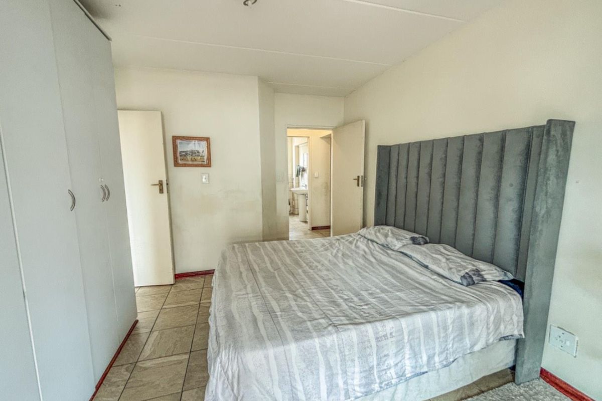 A bedroom featuring built-in cupboards and tiled flooring, with an adjoining bathroom visible through the doorway.