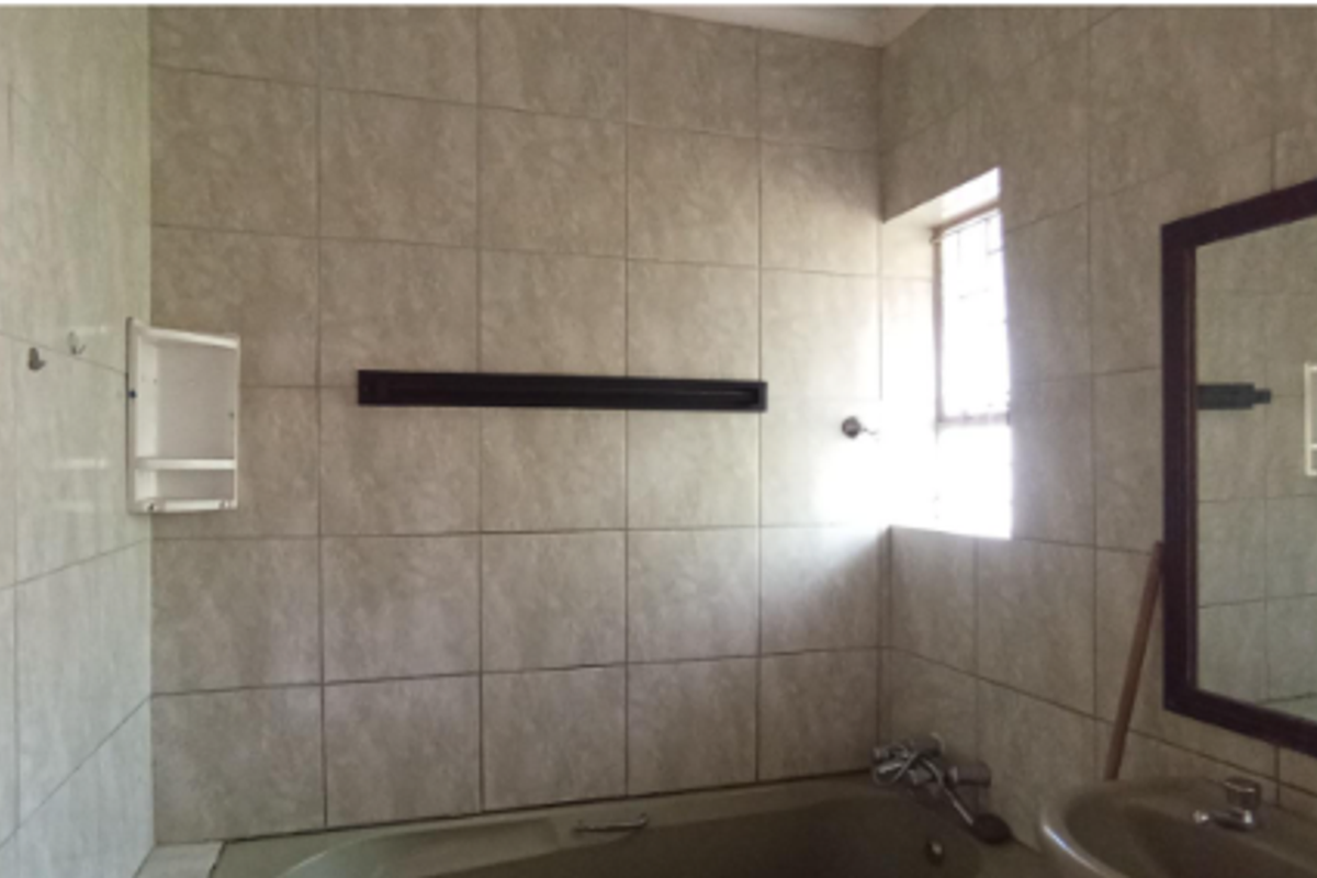 A functional bathroom featuring full-height wall tiling, a built-in bathtub, a wall-mounted mirror, and a window for natural light.