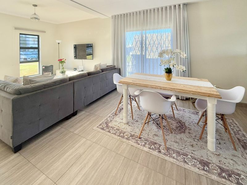 A bright and spacious open-plan living and dining area featuring large format floor tiles, neutral walls, and a sliding door leading to the exterior.