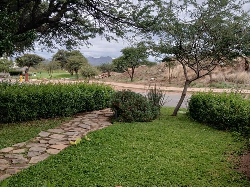 A well-maintained garden area featuring a stone pathway, lush green lawn, and mature trees with a scenic view of the surrounding landscape.
