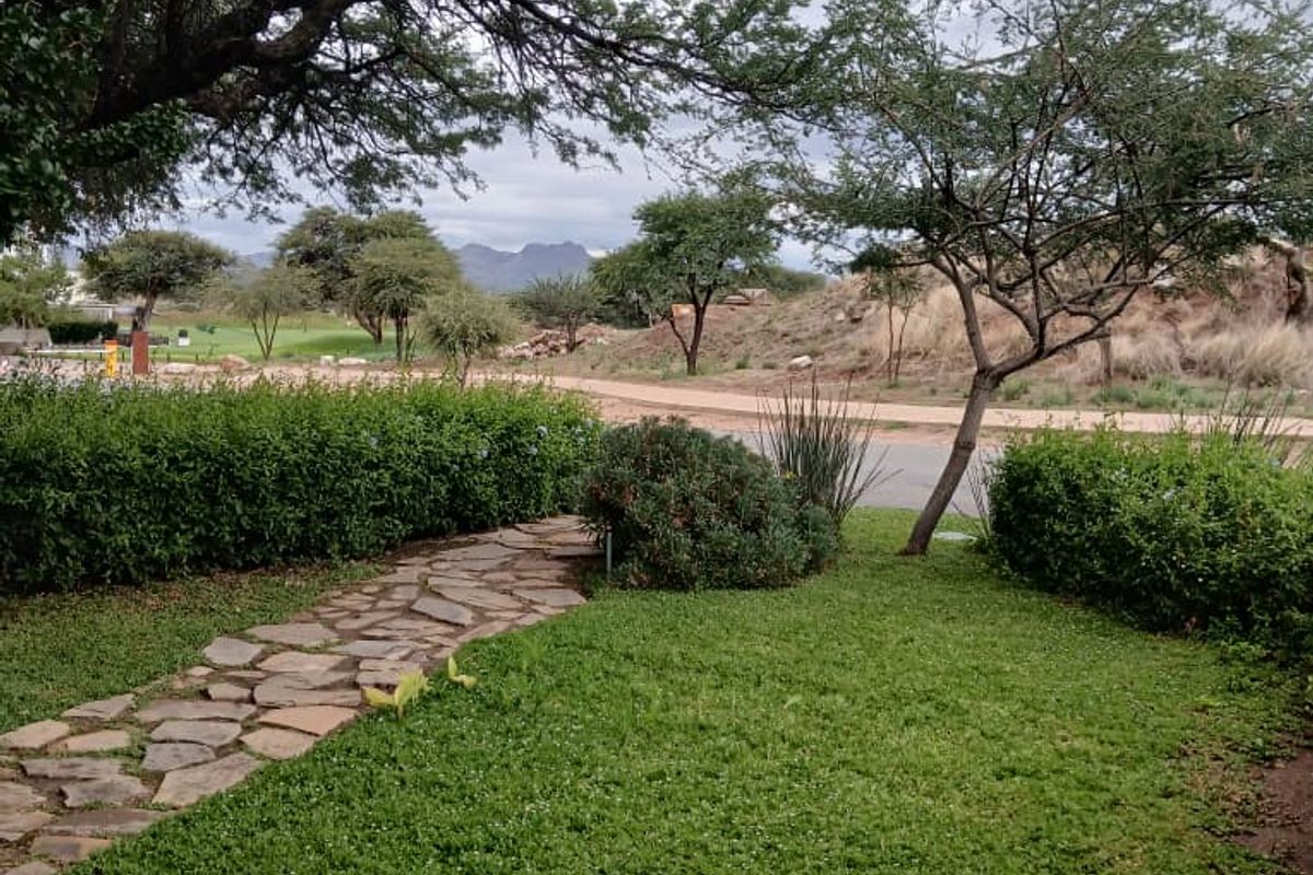A well-maintained garden area featuring a stone pathway, lush green lawn, and mature trees with a scenic view of the surrounding landscape.
