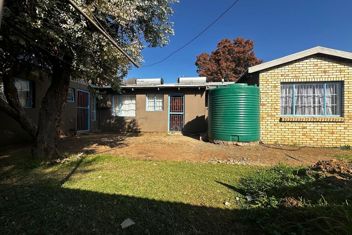 Rear view of the property featuring a brick and rendered facade, solar water heating systems, and a large water storage tank in the garden.