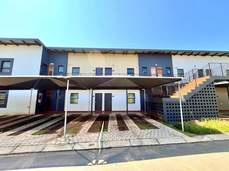 Front elevation of a modern apartment complex featuring covered parking bays, paved driveway, and external staircase access to upper units.