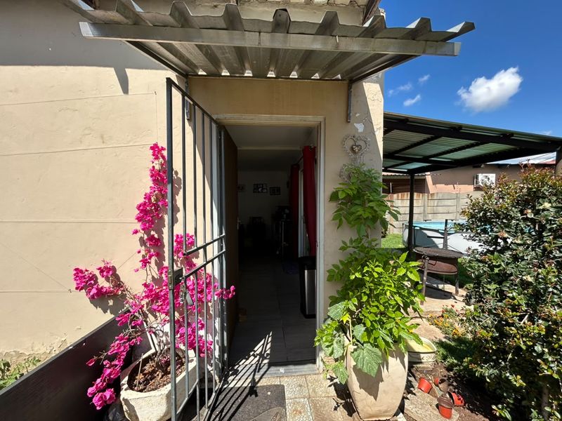 A covered patio area featuring a corrugated metal awning, security gate, and tiled flooring, providing access to the home's interior.