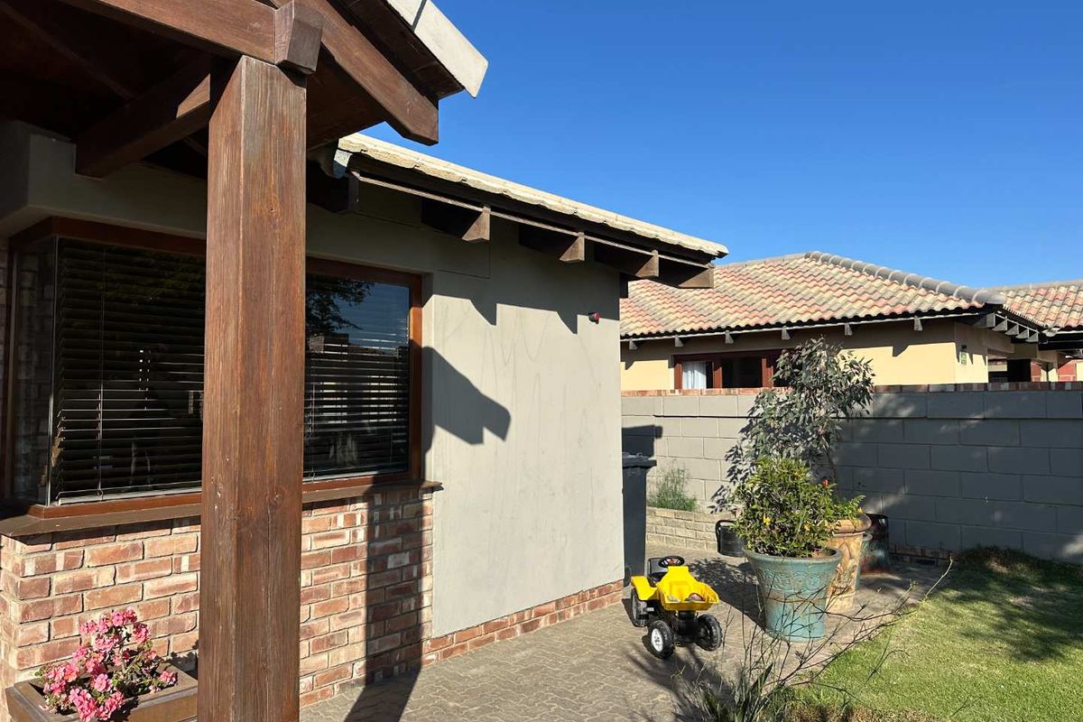 A view of the rear exterior featuring a covered patio area with timber support posts, brick accents, and a paved courtyard.