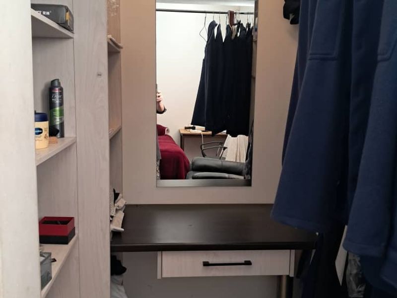 A walk-in closet or dressing area featuring built-in shelving, a vanity desk with a drawer, and a wall-mounted mirror.