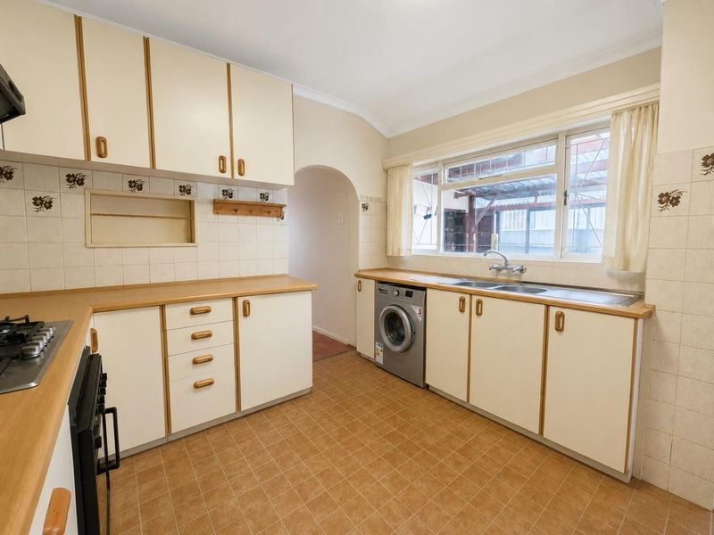 A functional kitchen featuring laminate countertops, built-in cabinetry, a gas cooktop, and a stainless steel sink with a view to the rear exterior.