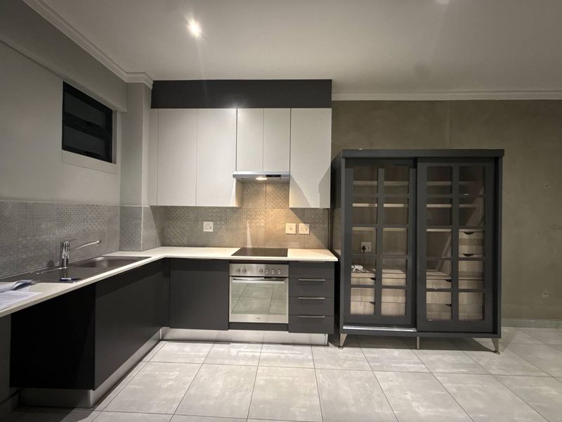 Modern kitchen featuring two-tone cabinetry, integrated oven and hob, tiled backsplash, and neutral floor tiles. The space is ready for final wall finishing.