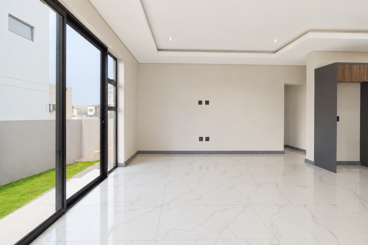 A bright, modern, and empty living area featuring large format marble-look floor tiles, recessed ceiling lighting, and expansive sliding glass doors leading to the garden.