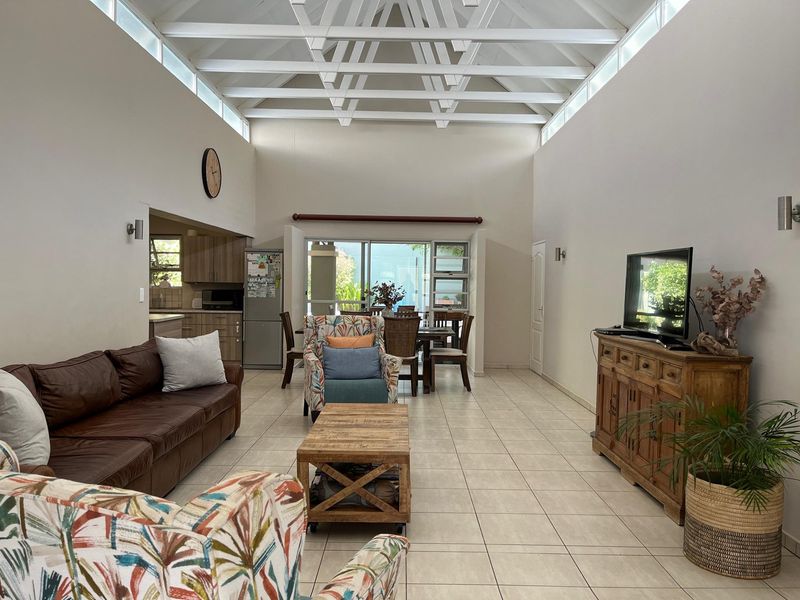 Spacious open-plan living and dining area featuring a high vaulted ceiling with exposed trusses, clerestory windows, and direct access to the outdoor patio.